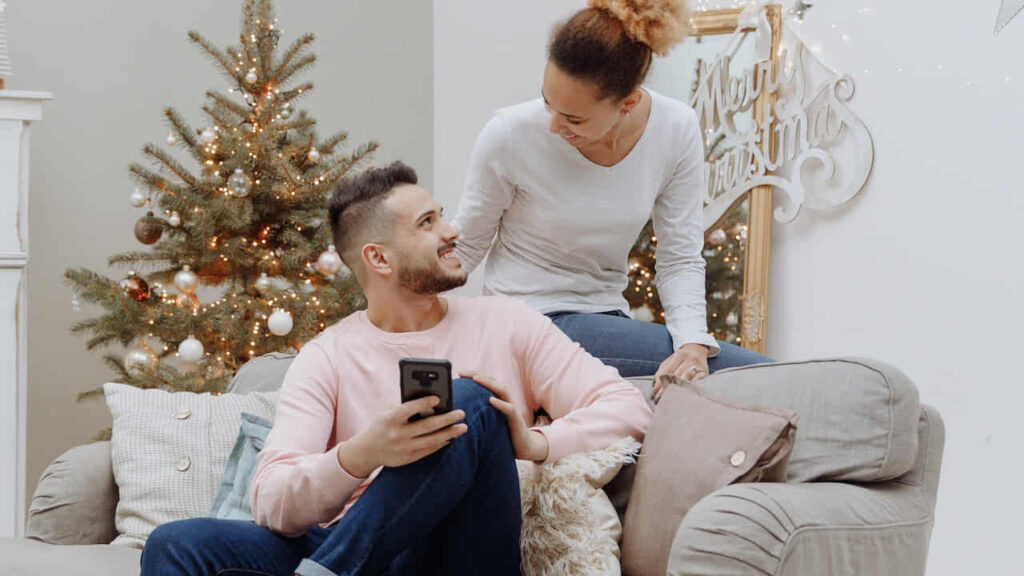 Couple on sofa with phone near Christmas tree