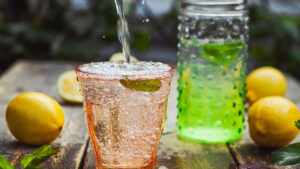 fizzy prebiotic soda being poured over ice with mint leaves, surrounded by fresh lemons