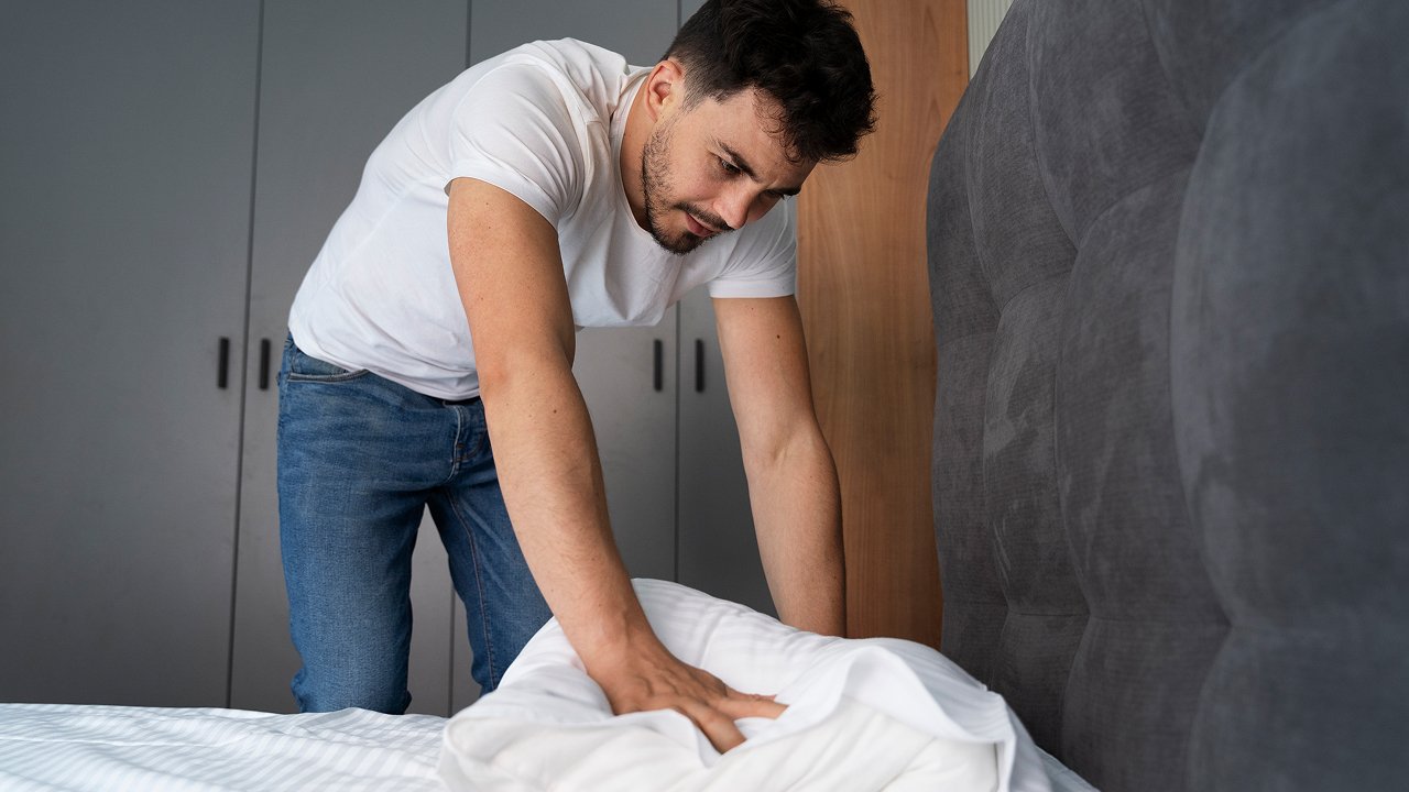 A man adjusting a bedsheet to prevent a mattress topper from sliding